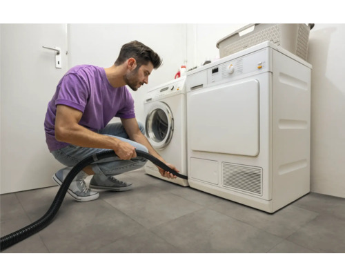 Muž čistí sušičku vysavačem ve světlé prádelně.