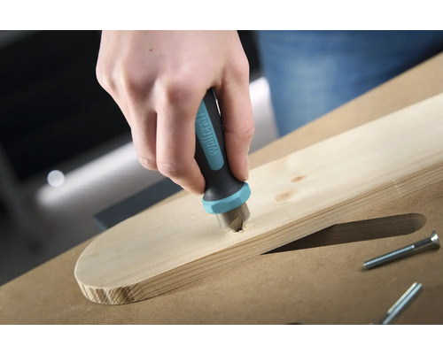 Ruka spouští zahlubovač značky Wolfcraft do dřevěné desky, aby zapustila šroub.