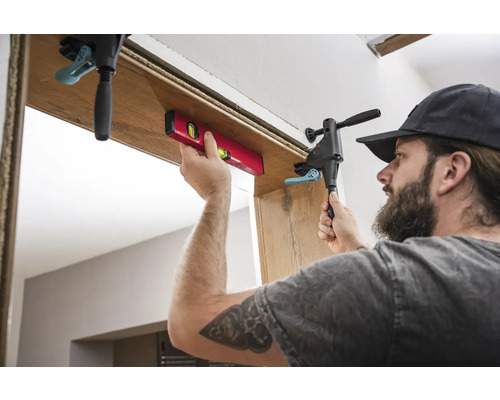 Řemeslník montuje zárubeň pomocí vodováhy a šroubové svorky.