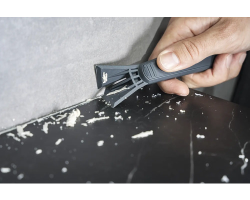 Osoba odstraňuje silikonové spáry mezi stěnou a povrchem pomocí škrabky na spáry.