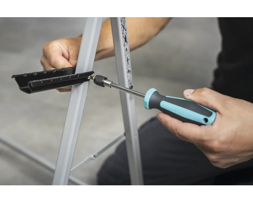 Osoba připevňuje černý díl k pracovnímu stolu pomocí šroubováku.