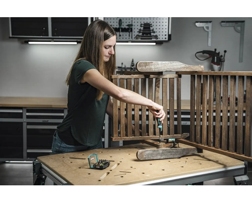 Žena montuje dřevěnou konstrukci šroubovákem v dílně