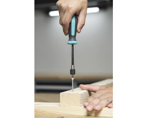 Osoba šroubuje šroub šroubovákem do dřevěné desky