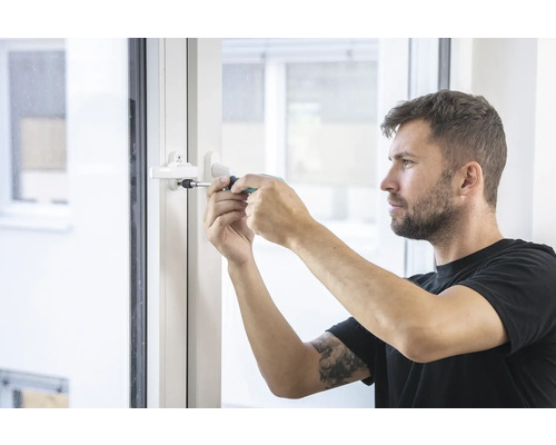 Muž opravuje okenní kliku pomocí šroubováku.