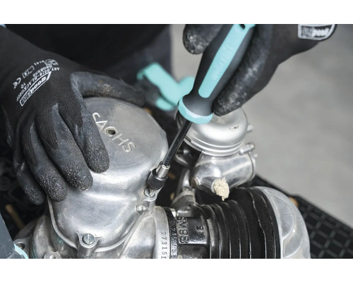 Osoba opravuje motor Sachs pomocí šroubováku.