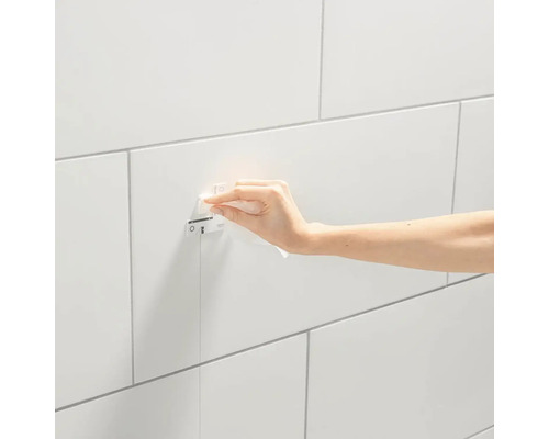 Ruka otírá ovládací panel Grohe na obložené stěně.
