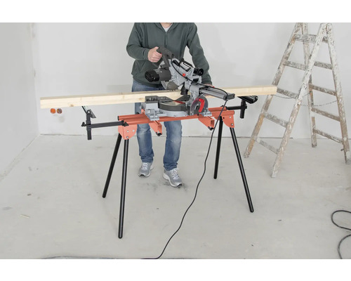 Osoba obsluhuje pokosovou pilu na řezacím stole vedle žebříku.