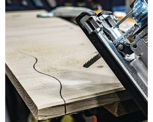 Detailní záběr přímočaré pily řezající zakřivený vzor do dřevěné desky