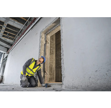 Stavební dělník s ochrannou přilbou a bezpečnostní vestou měří dveřní otvor laserovým dálkoměrem.