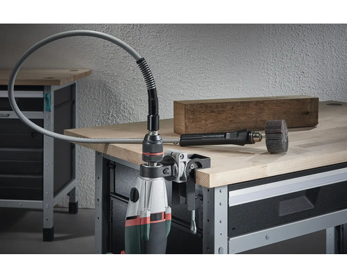 Vrtací stroj s namontovaným ohebným hřídelem a brusným nástrojem na pracovním stole