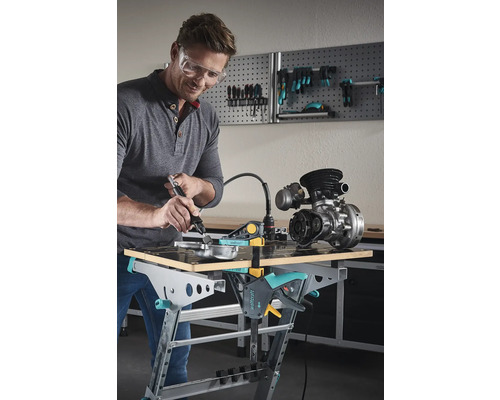 Muž s ochrannými brýlemi opracovává kovový díl na ponku Wolfcraft pomocí multifunkčního nástroje.