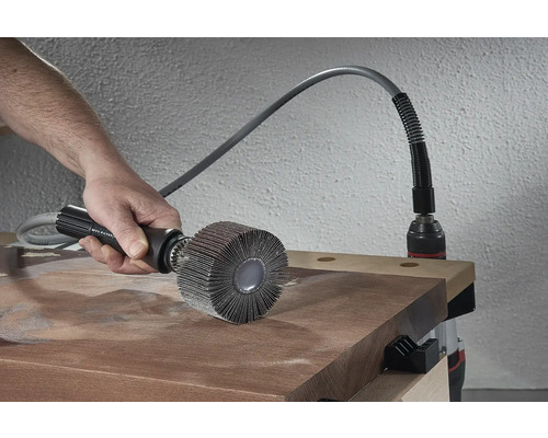 Osoba používá lamelový kartáč na dřevěné desce, poháněný vrtačkou.