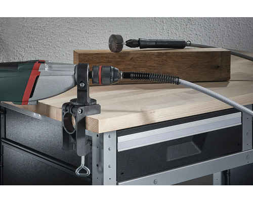 Vrtací stroj s namontovanou stolní svorkou a ohebným hřídelem na pracovním stole.