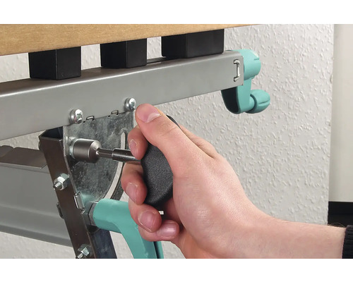 Osoba připevňuje šroub šroubovákem k rámu kovové postele.