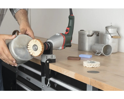 Osoba leští nádobu lešticím strojem na pracovním stole.