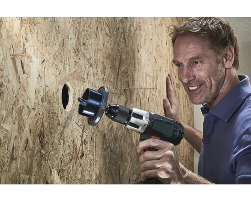 Muž vrtá děrovkou otvor do dřevěné stěny.