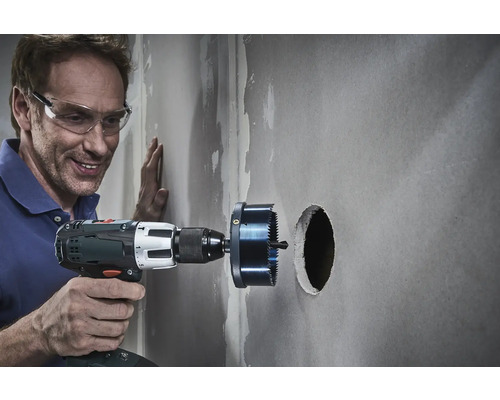 Řemeslník vrtá otvor do zdi pomocí děrovky