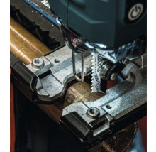 Detailní pohled na přímočarou pilu řezající kovovou trubku.