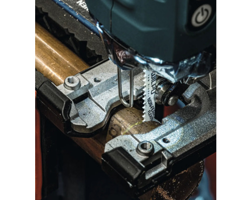 Detailní pohled na přímočarou pilu řezající kovovou trubku.