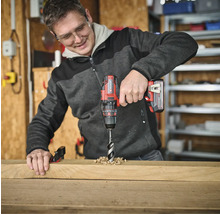 Muž vrtá otvor do dřevěné desky pomocí akumulátorového šroubováku.