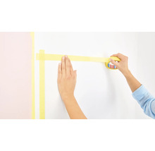 Osoba lepí malířskou pásku na zeď.