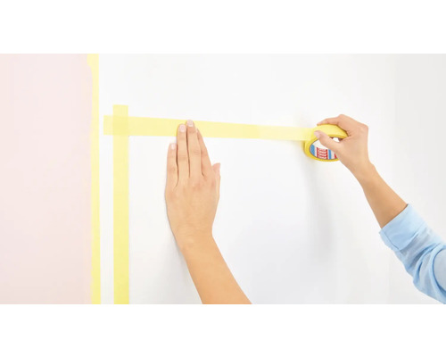 Osoba lepí malířskou pásku na zeď.