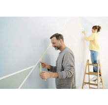 Dvě osoby zdobí stěnu maskovací páskou a geometrickými tvary.