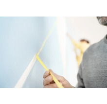 Muž upevňuje malířskou krepovou pásku na zeď