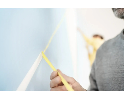 Muž upevňuje malířskou krepovou pásku na zeď