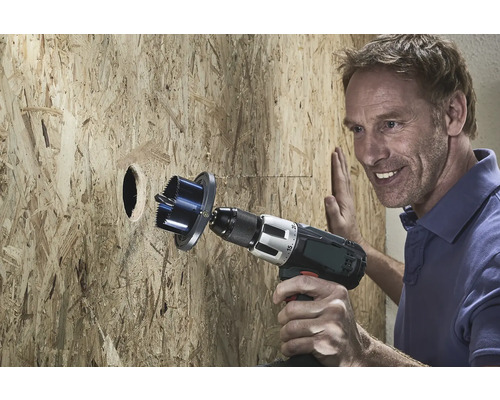 Muž vrtá otvor do dřevěné desky pomocí děrovky.