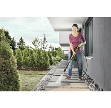 Žena čistí chodníkové desky vysokotlakým čističem na zahradě.