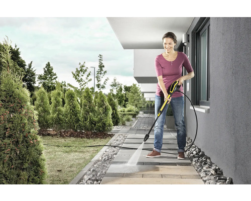 Žena čistí chodníkové desky vysokotlakým čističem na zahradě.