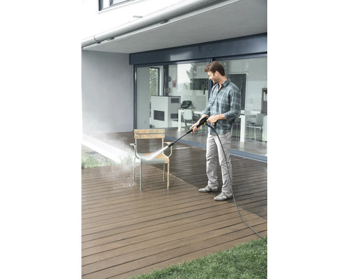 Muž čistí židli vysokotlakým čističem na terase.