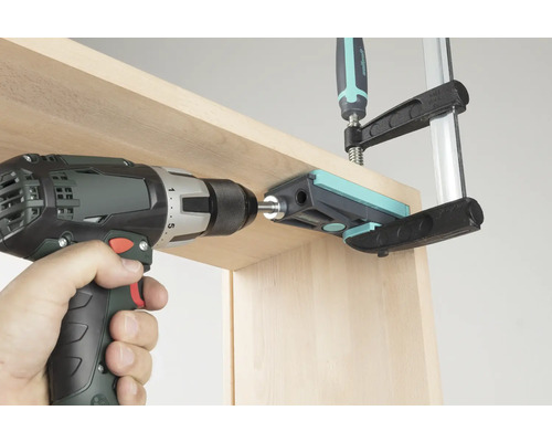 Akumulátorový šroubovák vrtá skrz vrtací šablonu do dřevěné desky