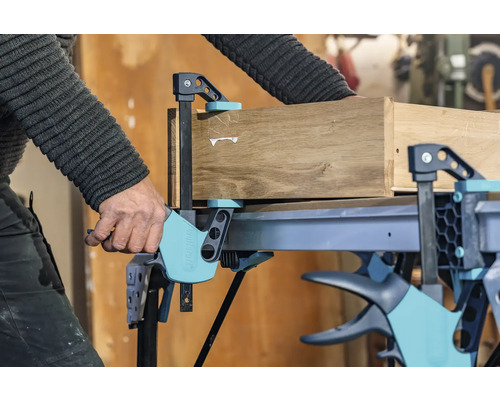 Řemeslník upevňuje dřevo jednou rukou svěrkou na pracovní stůl