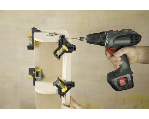 Dílenská scéna zobrazuje dřevěný roh upevněný úhlovými svorkami a sešroubovaný akumulátorovým šroubovákem.