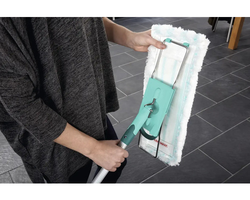 Osoba drží mop s omyvatelným návlekem. Mop má teleskopickou tyč a otočnou hlavici k čištění podlah.