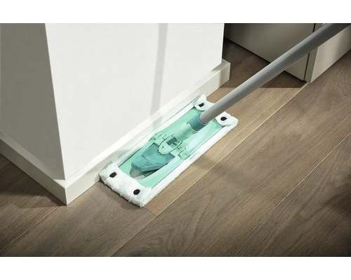 Mop s návlekem z mikrovlákna čistí dřevěnou podlahu u bílé zdi.