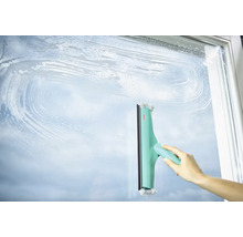 Ruka čistí skleněný povrch stěrkou na okna