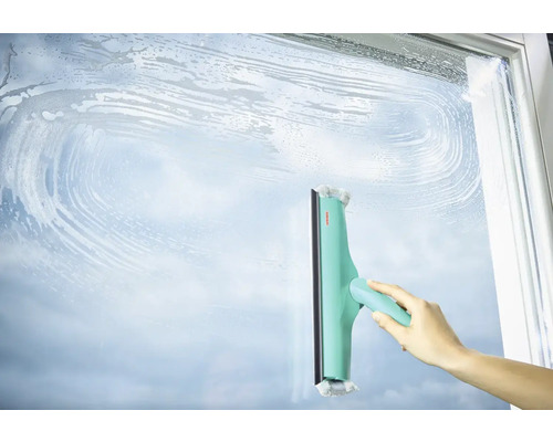 Ruka čistí skleněný povrch stěrkou na okna