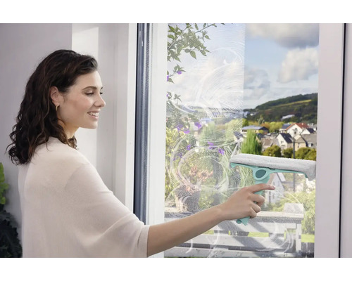 Žena čistí okna stěrkou pro čištění beze šmouh