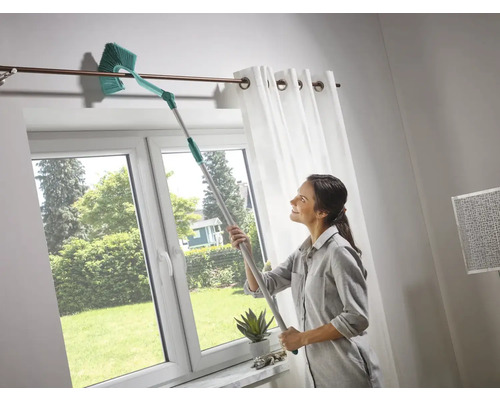 Žena čistí záclonovou tyč teleskopickým prachovkou ve světlé místnosti