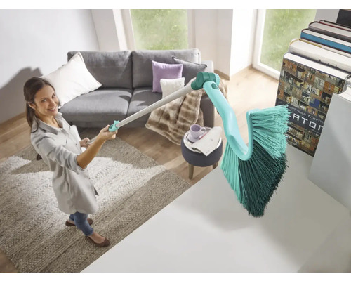 Žena používá kartáč s rukojetí k úklidu v obývacím pokoji.