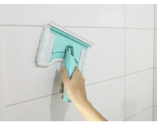 Ruka používá stěrku na okna s návlekem z mikrovlákna na obkládané stěně