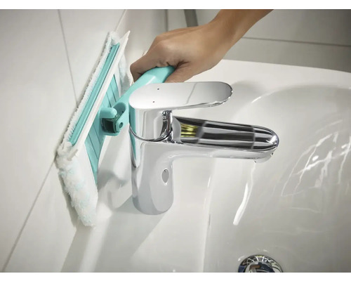 Čištění stěny koupelny s koupelnovou stěrkou vedle umyvadla.