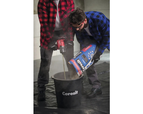 Dva řemeslníci míchají lepidlo na dlaždice ve vědru pomocí míchadla