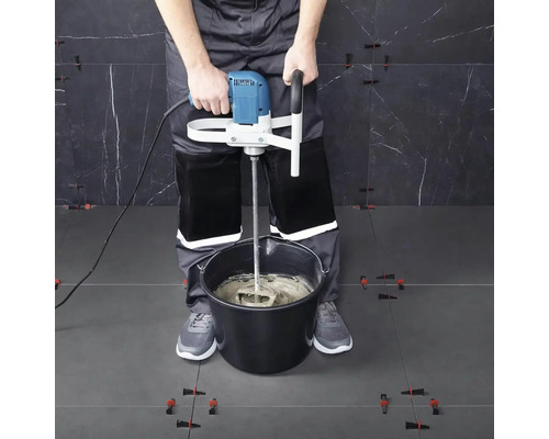 Řemeslník míchá lepidlo na obklady míchadlem ve vědru.