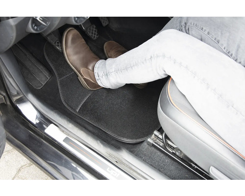 Interiér vozidla s podlahovou rohoží a nohou na pedálu