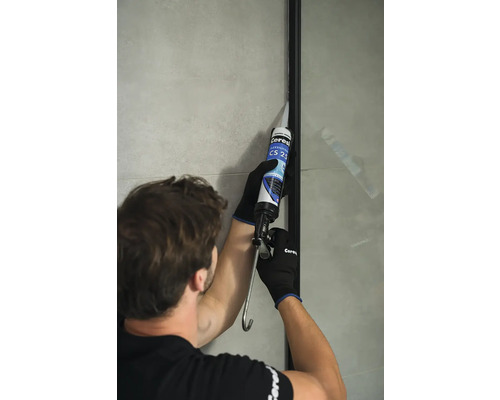 Řemeslník utěsňuje sprchovou stěnu silikonem. Viditelné logo Ceresit.