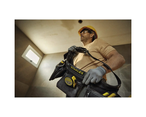 Řemeslník s brašnou na nářadí Stanley a svinovacím metrem na staveništi